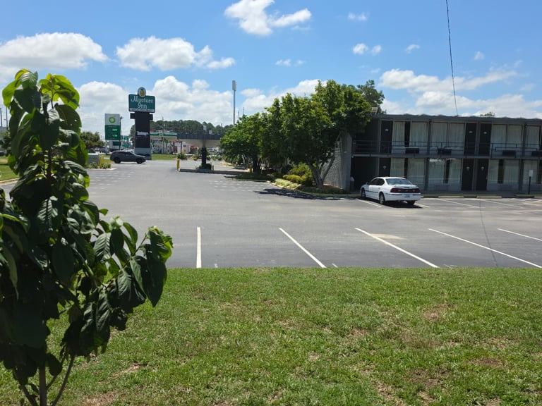 The Masters Economy Inn pineapple sign and parking lot with the guest room building alongside US Highway 70 East